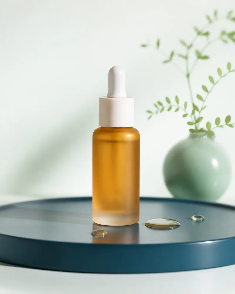 Amber facial oil dropper bottle on a teal tray beside a mint vase